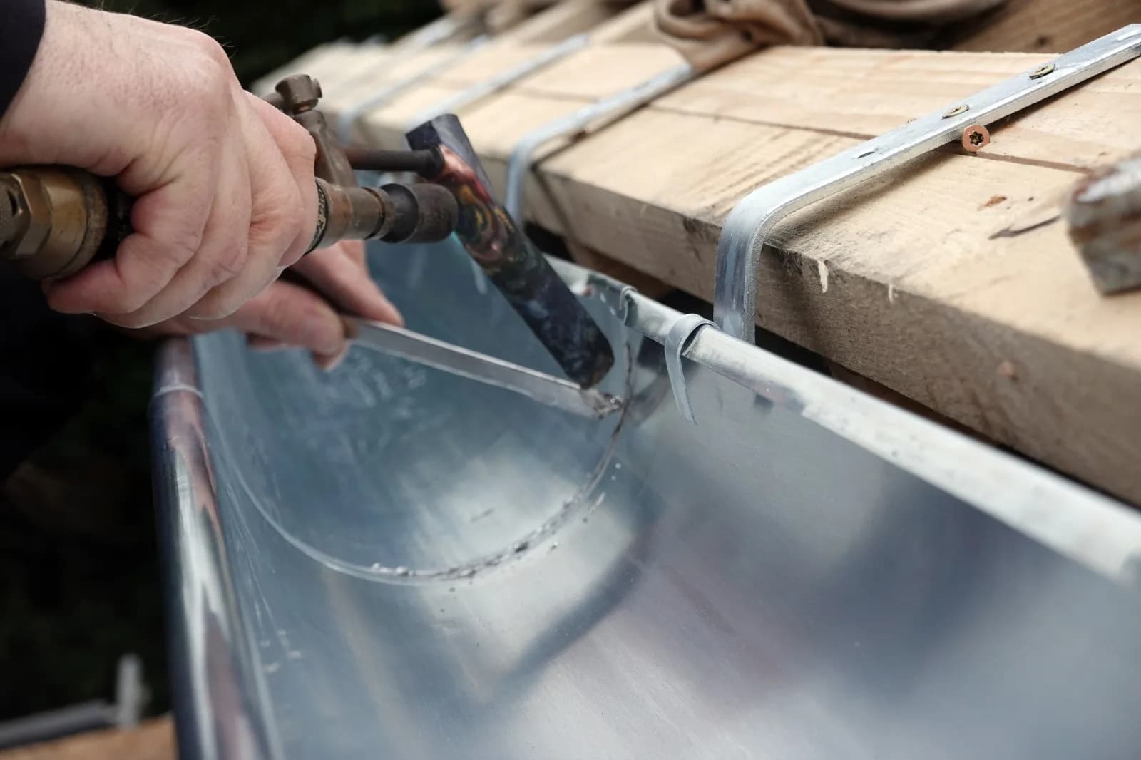 Bauklempnerarbeit an einer Dachrinne mit Loetgeraet
