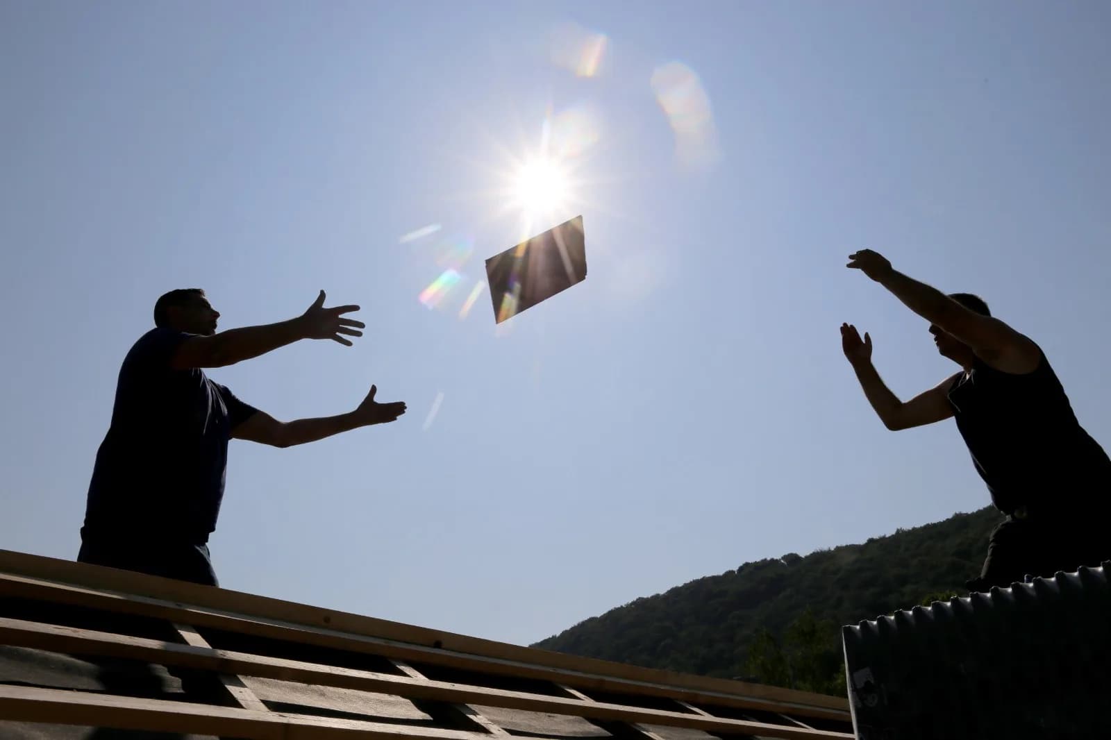 Zwei Dachdecker reichen sich Material auf dem Dach als Zeichen für eingespielte Teamarbeit
